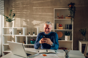 Middle aged man working in a home office and using smartphone