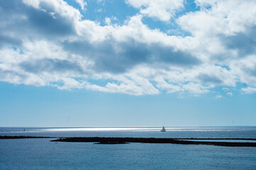 Fototapeta premium Seascape and cloudscape in blue color. Calm sea on a sunny day with clouds horizontal landscape background. Distant boat silhouette in the ocean.