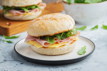 Two homemade sandwiches with ham, cheese and arugula on a concrete table.