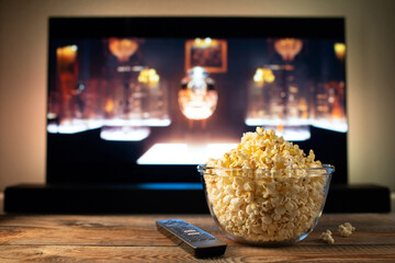 A glass bowl of popcorn and remote control in the background the TV works. - obrazy, fototapety, plakaty