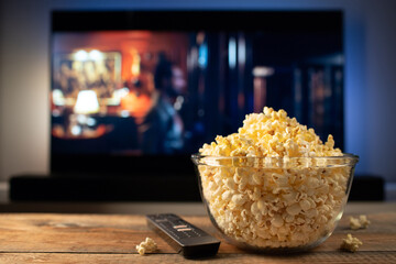 A glass bowl of popcorn and remote control in the background the TV works.