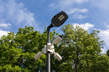 Modern lamppost and 3 surveillance cameras mounted in different directions in public park. Public...