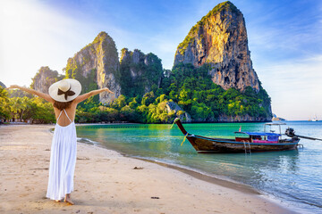 A happy tourist woman in a white summer dress stands on the beautiful beach of Railay at the Krabi...