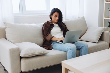 Fototapeta premium Woman freelancer on day off sitting on sofa with laptop at home online shopping on internet, smile