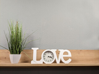 on a wooden shelf there is a green flower in a pot and a clock in the inscription love
