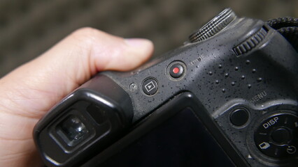 Close-up shot of a person holding a digital camera. A hand holding a DSLR camera. Digital camera details: tiny camera buttons. A photographer holding a camera.