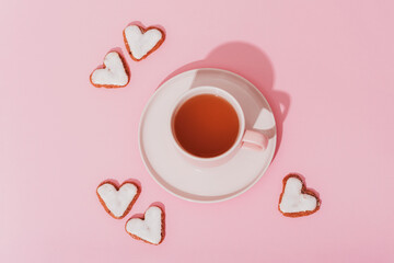 A cup of tea and heart-shaped cookies on pink background in sunlight. Valentines day concept. Top...
