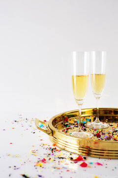Champagne flutes in tray with confetti on table against white background