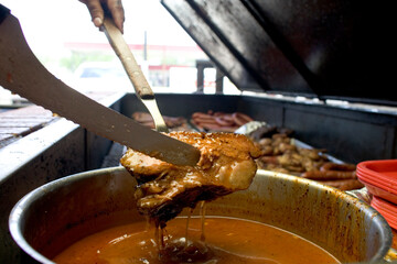 A beef brisket held by tongs about to be dipped in sauce at a restaurant in Llano, Texas.