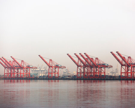 A row of red cranes at the water edge at the Ports of Long Beach and Los Angeles, California.