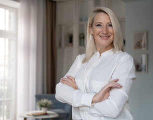 Smiling confident stylish mature middle aged woman standing at home office.