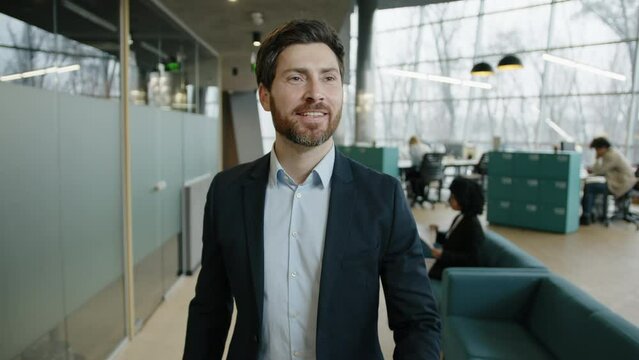 Portrait of successful manager looking happy while his colleagues working in the background. Close-up shot of a smiling caucasian man wearing formal businesswear in the office. High quality 4k footage