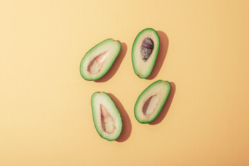 Halves of avocado on yellow background with sharp shadows. Healthy vegan food concept. Top view,...