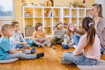 Kindergarten teacher with children sitting on the floor having music class, using various...