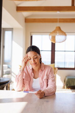 Image of biracial woman holding pregnancy test sitting at table at home