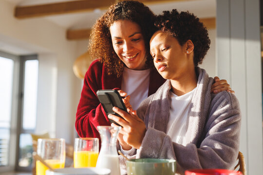 Happy diverse lesbian couple using smartphone in kitchen