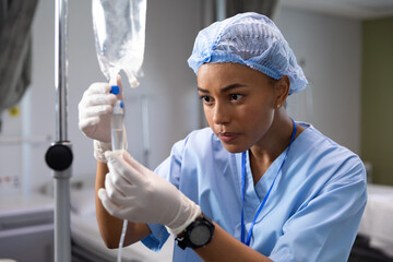 Biracial female doctor working at hospital, changing a drip