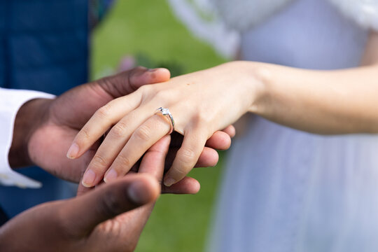 Hands of diverse groom and bride wearing wedding ring at outdoor wedding, copy space
