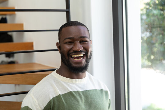 Happy african american man standing by window, laughing to camera, copy space