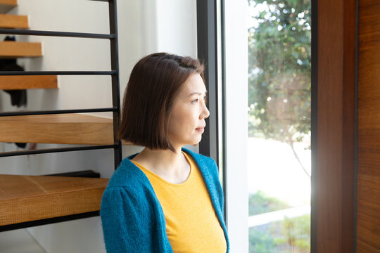 Thoughtful asian woman standing, looking out of living room window, copy space
