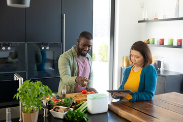 Happy diverse couple cooking together, using tablet and composting waste in kitchen, copy space
