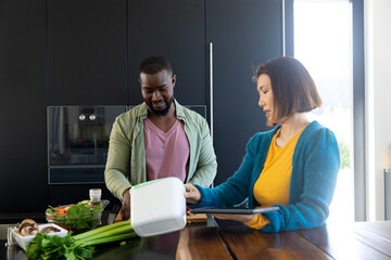 Happy diverse couple cooking, using tablet and composting waste in kitchen, copy space