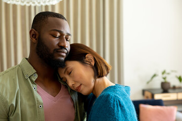 Thoughtful, happy diverse couple embracing with eyes closed in living room at home
