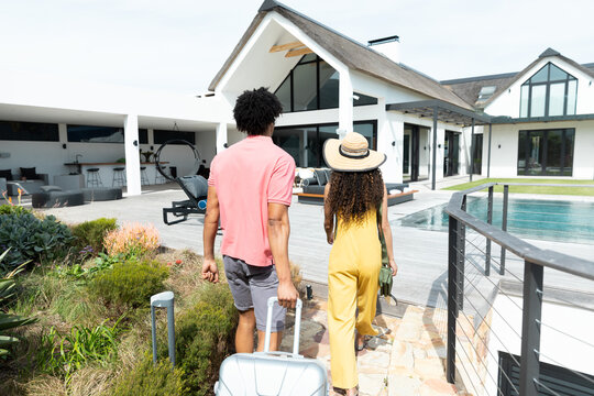 Rear view of biracial couple arriving outside holiday home with luggage, copy space