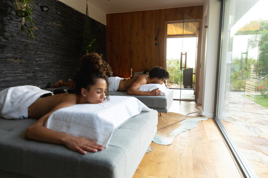 Relaxed biracial couple on massage tables having hot stones treatment at health spa, copy space