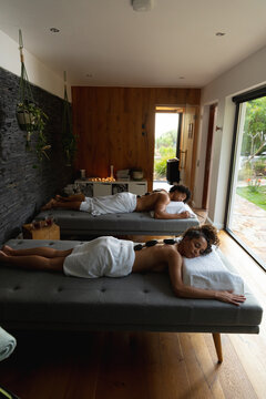 High angle view of biracial young couple with hot stones on backs lying on bed in spa