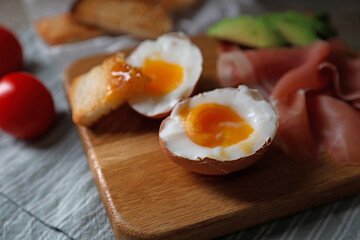 Delicious breakfast with soft boiled egg and tasty prosciutto on table, closeup