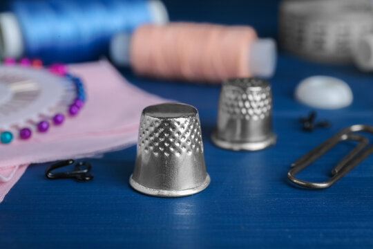 Silver thimble on blue wooden table, space for text. Sewing accessories - Powered by Adobe