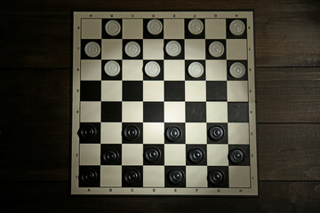 Checkerboard with game pieces on wooden table, top view