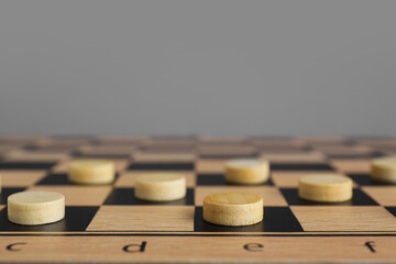Wooden checkerboard with game pieces on light grey background, closeup