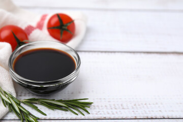 Bowl with balsamic vinegar, rosemary and tomatoes on white wooden table. Space for text