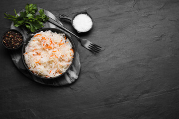 Bowl of tasty sauerkraut and ingredients on black table, flat lay. Space for text