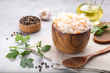 Bowl of tasty sauerkraut and ingredients on grey table
