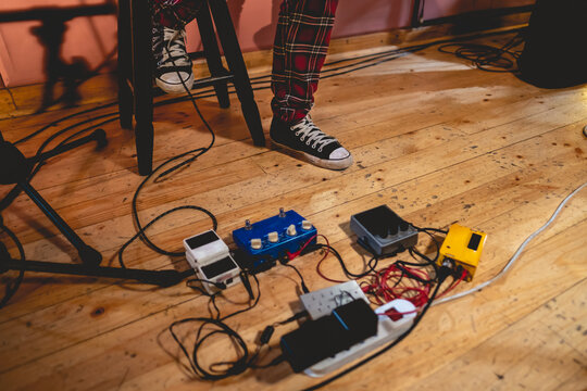 Legs And Feet Of A Person With Black Sneakers And Red Vintange Quadrille Pants Next To Several Colorful Guitar Pedals Over Wood Floor