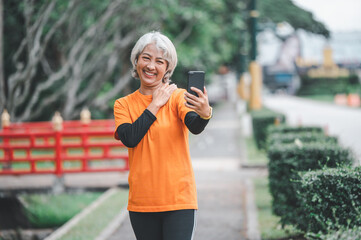 Elderly white haired Asian woman talking Video call while exercising in the park in the morning.