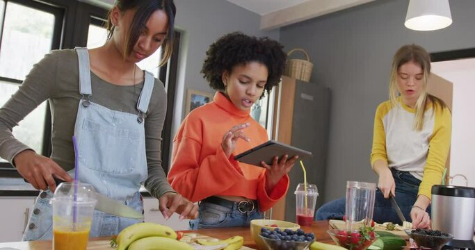 Diverse teenager girls friends cutting fruit and using tablet in kitchen, slow motion