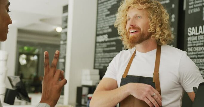 Happy Diverse Woman Buying Coffee And Talking With Male Barista In Cafe