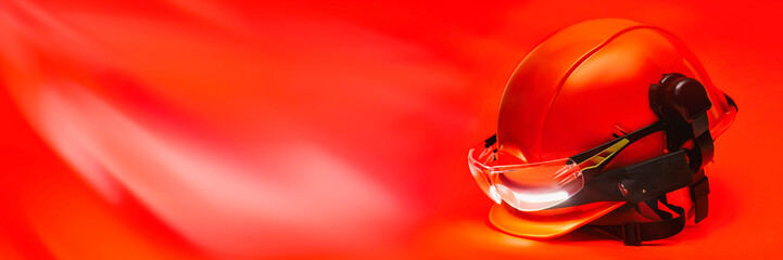Protective goggles for eyes and construction helmet for head with earmuffs and headlamp on a red background. Construction tool and form for protection. © vadish