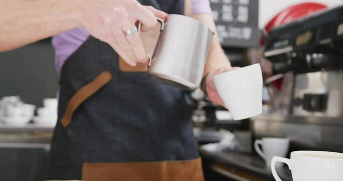 Caucasian male barista wearing apron adding milk to coffee in cafe