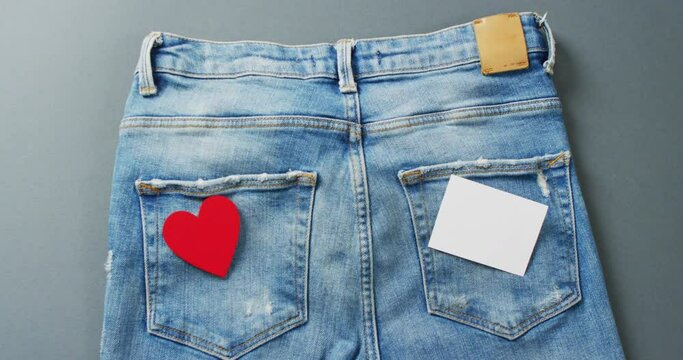 Close up of jeans with heart and white note on grey background with copy space