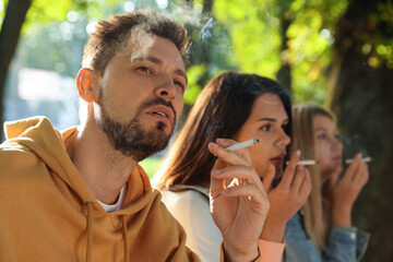 People smoking cigarettes outdoors on sunny day