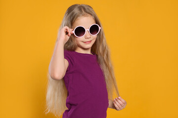 Girl in stylish sunglasses on orange background