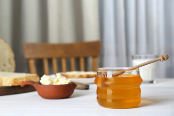 Jar with honey, butter, bread and milk served for breakfast on white wooden table