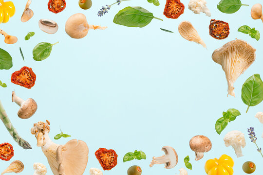 Natural frame made with oyster mushrooms, champignons, herbs and vegetables floating above isolated pastel blue background. Mediterranean diet concept. Minimal creative pattern. Healthy food texture.