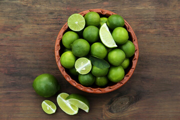 Whole and cut fresh ripe limes in bowl on wooden table, flat lay