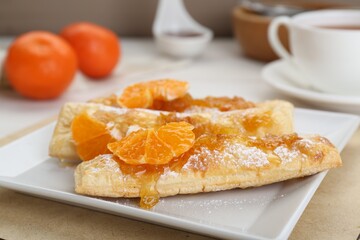 Fresh tasty puff pastry with sugar powder and tangerines on table, closeup